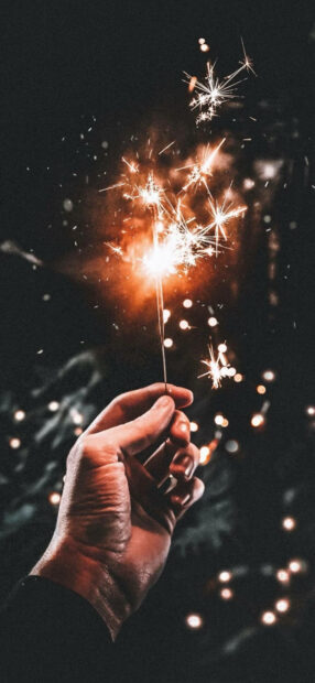 New Years Eve Wallpaper showing a hand holding a bright sparkler with golden sparks against a dark, bokeh background