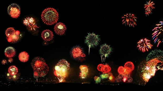 A lively New Years Eve Wallpaper showcasing a scattered display of colorful red and green fireworks against a dark sky