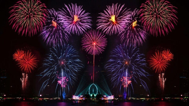 A stunning New Years Eve Wallpaper showcasing a symmetrical fireworks display over a city harbor at night