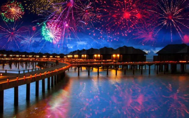 A breathtaking New Years Eve wallpaper displaying tropical overwater bungalows with colorful fireworks reflecting on the water