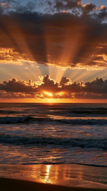 An Ocean Wallpaper featuring a dramatic sunset over the sea with golden sun rays piercing through dark clouds above crashing waves on a beach