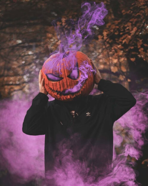 A person wearing a carved pumpkin head with purple smoke emanating from it creates a unique Halloween Macbook wallpaper