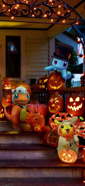 This Pokemon Halloween Wallpaper shows Charmander, Squirtle, and Pikachu in costumes on a pumpkin-decorated porch with string lights