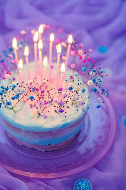 A vibrant Birthday Wallpaper featuring a layered cake with lit pink candles and tiny colorful flowers on a purple background