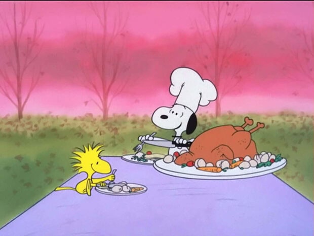 A classic Snoopy fall wallpaper showing Snoopy as a chef carving a Thanksgiving turkey with Woodstock, set against a pink autumn sky and bare trees