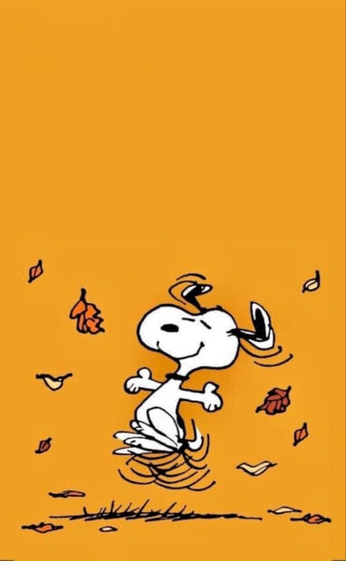 A delightful Snoopy Fall Wallpaper showing Snoopy dancing joyfully amidst falling autumn leaves on a vibrant orange background
