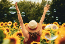 A joyful person with a straw hat in a field of vibrant sunflowers with floating bubbles, perfect for a Summer Aesthetic Wallpaper