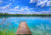 A serene Summer Vibes Wallpaper with a wooden pier extending into a clear blue lake under a bright sky