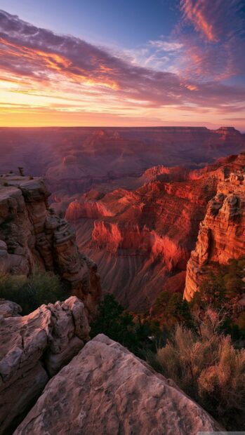 A breathtaking Sunset Wallpaper of the Grand Canyon, showcasing rugged cliffs bathed in warm light under a vibrant orange and purple sky