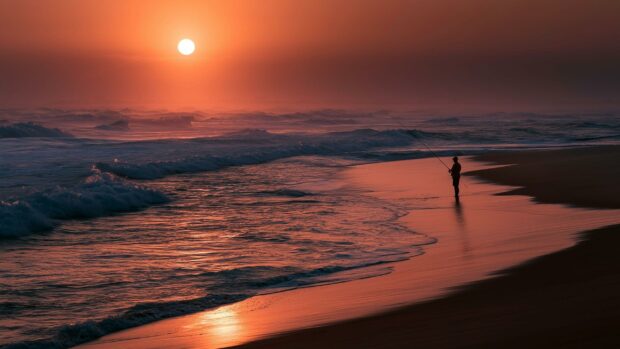 A striking beach wallpaper depicting a lone fisherman on the shore against a vivid red sunset sky and crashing waves
