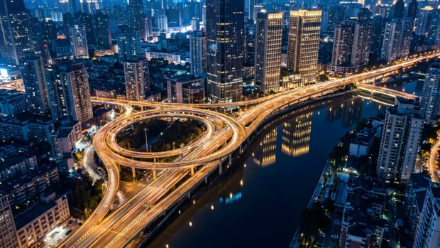 A stunning aerial view City Wallpaper featuring a modern city skyline at night with a complex highway interchange and a river