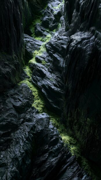 A dark aesthetic wallpaper featuring a deep, narrow canyon with dark, jagged rock formations and vibrant green moss growing along the path