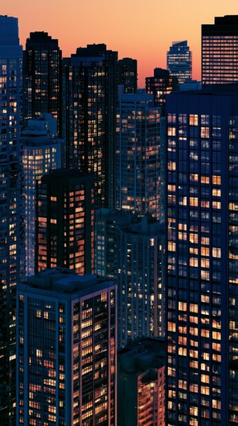 Dark wallpaper featuring a night cityscape with numerous tall buildings and illuminated windows against a sunset sky