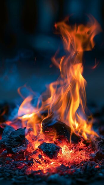 A vertical fire wallpaper showing intense orange flames burning on dark red embers with blue smoke in the background