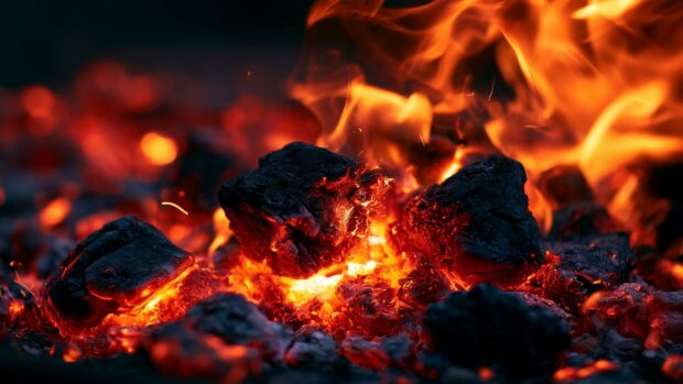 Macro fire wallpaper showcasing a close-up of intensely burning coals and glowing embers with soft flames in the background
