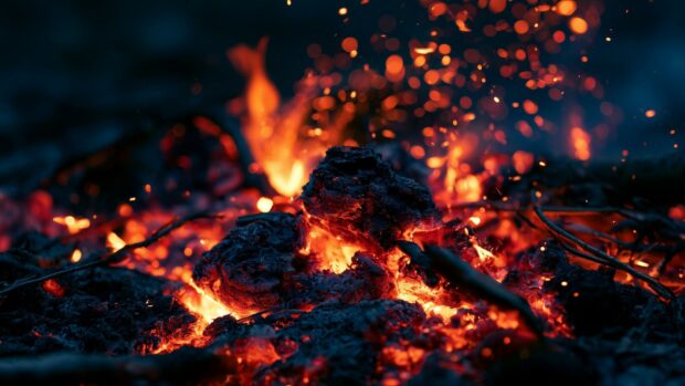 A horizontal fire wallpaper with a close-up view of glowing red embers, flying sparks, and blurred fire in the background