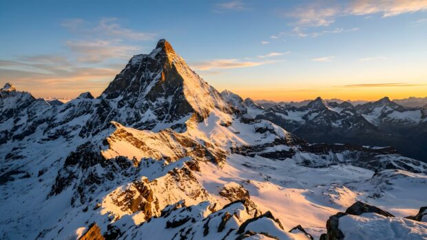 A stunning landscape wallpaper featuring a snow-capped mountain peak illuminated by a golden sunrise