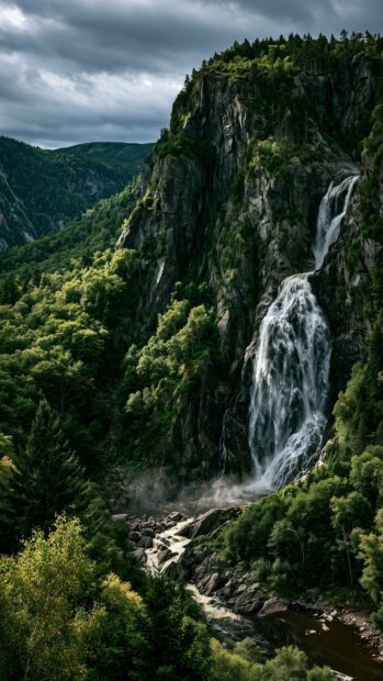 A dramatic mountain wallpaper showcasing a powerful waterfall cascading down a steep, tree-covered cliff amidst a lush green forest
