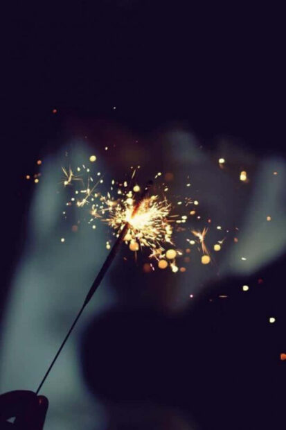 A New Year Aesthetic Wallpaper showing a bright sparkler burning in the dark with warm bokeh lights in the background