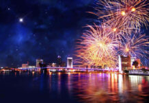 A stunning New Year Aesthetic Wallpaper featuring a city skyline at night with vibrant fireworks exploding over the water and a shooting star in the dark sky