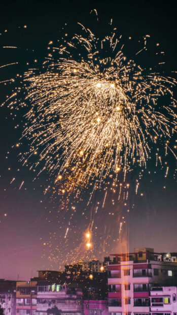 A captivating New Year aesthetic wallpaper featuring a grand fireworks display lighting up the night sky above a bustling city skyline
