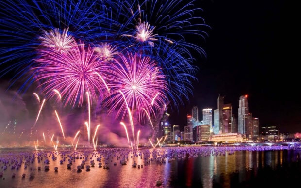 A stunning New Year Aesthetic Wallpaper showing colorful fireworks exploding over a city skyline with reflections in the water