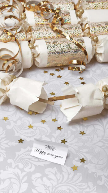 A New Year Aesthetic Wallpaper featuring gold and white party crackers with scattered star confetti and a "Happy New Year" card on a patterned tablecloth