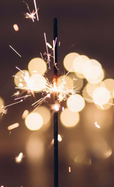 A New Year Aesthetic Wallpaper showcasing a vibrant sparkler with large, soft bokeh lights creating a warm background effect