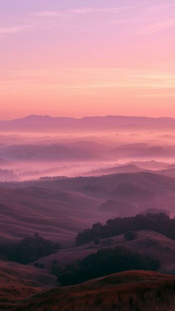 A beautiful pink aesthetic wallpaper showing foggy mountain peaks at sunset with a gradient sky