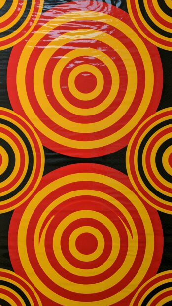 A vibrant retro wallpaper featuring a repeating pattern of concentric red and yellow circles on a black background