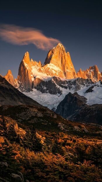A dramatic mountain peak illuminated by sunset light against a dark sky