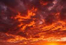 A stunning red aesthetic wallpaper of a sunset over a beach with footprints in the sand
