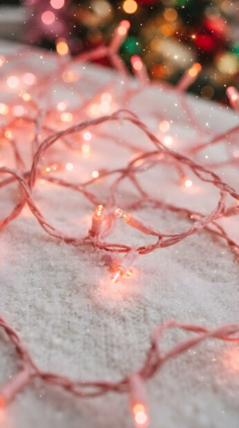 A cute pink Christmas wallpaper features string lights scattered on a snowy surface