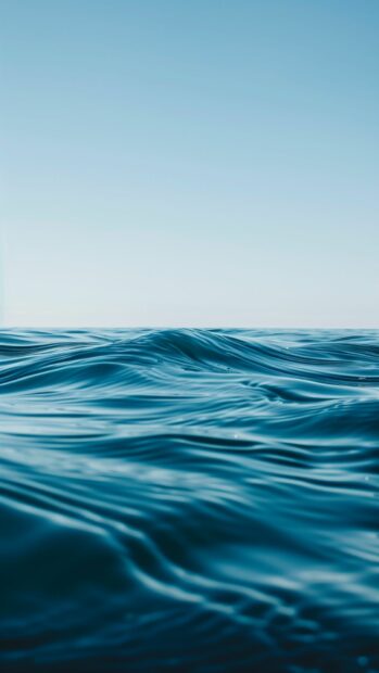 A calm ocean with a bright blue sky and gentle waves, iPhone wallpaper.