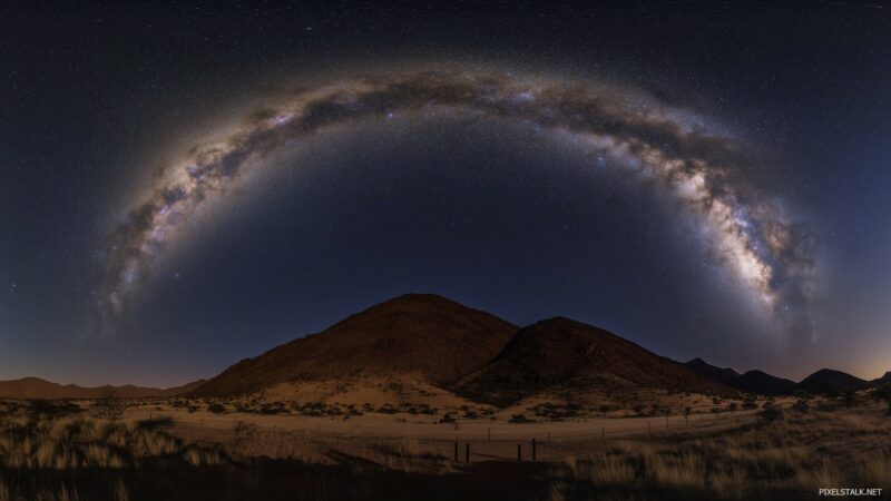 Starry night sky with the Milky Way arcing over mountain hills.