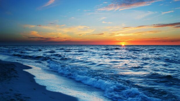 Sunset over ocean with colorful sky and waves, tranquil beach scene, evening coastal view.