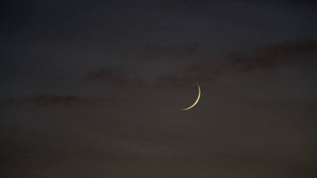 Crescent moon on night sky with clouds passing by full.