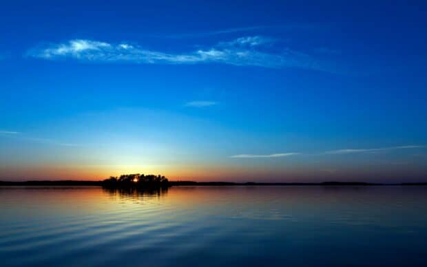 Serene lake at sunset with calm water and blue sky.
