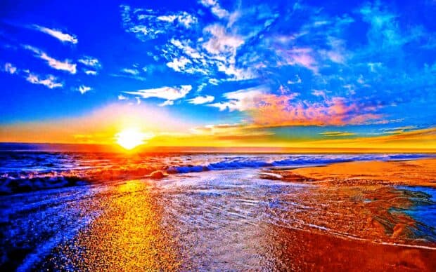 Vibrant sunset over colorful ocean beach with dramatic sky and shimmering water.