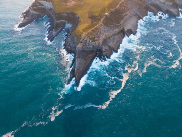 Cliffs along rugged coastline with waves crashing below, captured from an aerial view.