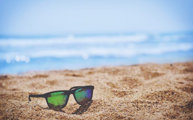 Sunglasses on beach sand during Summer daytime.