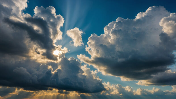 Summertime sky with a bright sun shining through fluffy white clouds.